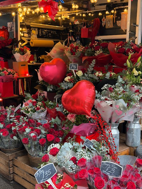 A vibrant display of floral arrangements at the flower stall, featuring a range of red and white roses, baby's breath, and greenery wrapped in clear and white paper. Prominent among the blooms are sev