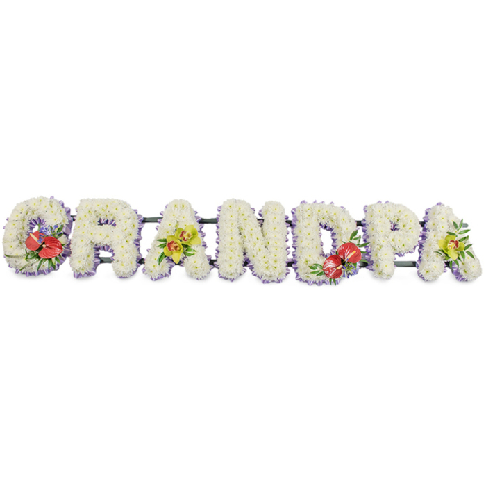 A serene and meaningful floral arrangement spells out "GRANDPA" in bold, three-dimensional capital letters, displayed against a clean white background that allows the textures and colours to stand out clearly. Each letter is built from a dense covering of small white chrysanthemums, the blooms arranged so closely that they form a continuous, plush surface, almost like snow that has just settled. The soft white petals suggest peace, innocence, and the quiet of a chapel before mourners arrive. A fine trim of pale lavender ribbon runs along the base of each letter, its subtle lilac tone adding delicate contrast and a sense of careful craftsmanship, the way a local florist near Lower Clapton Road might finish a bespoke funeral tribute. The entire word rests on discreet dark green bars that provide stability and a subtle grounding line beneath the flowers. Accents of stronger colour are placed with compositional balance and emotional intent. On the "G" and the "D", clusters of deep red anthuriums with their waxy, heart-shaped blooms and yellow spadices sit among glossy green leaves and small purple filler flowers, providing rich focal points that speak of love, respect, and the intensity of farewell. On the first and last "A", elegant stems of yellow-green orchids rise from the chrysanthemums, their slender, arching shapes and intricate, speckled faces adding a refined beauty and a hint of gentle optimism. The tribute feels both formal and deeply personal, well suited to a grandfather's funeral or celebration of life in Lower Clapton, whether placed in a church near Clapton Pond or at a crematorium chapel further across Hackney. Through flower choice, colour harmony, and precise handwork, the design becomes a heartfelt message of remembrance and gratitude for a much-loved grandpa.