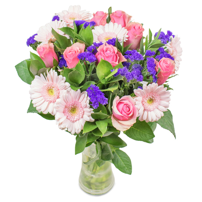 Centrally displayed in a clear glass vase, this vibrant bouquet from Lower Clapton presents a stunning medley of pink roses and gerbera daisies-each bloom carefully selected and arranged by an experienced local florist. The roses, numbering around seven to nine, vary from tightly wound buds to those just beginning to reveal their spiraled mystery, their soft to medium pink petals suggesting a sense of anticipation and romance. Five to seven pale pink gerberas encircle the arrangement, their large faces and numerous silky petals glowing with a touch of sunlight that catches through the studio windows near Clapton Square. Striking purple filler flowers-likely statice-intertwine throughout, introducing cool visual depth and lively texture evocative of spring along the River Lea. Luxurious, deep green foliage brims from the base, offering lushness and a breath of verdant freshness that recalls local parks in the early morning. The transparent vase, with its visible stems and sparkling water, lends a contemporary clarity, reinforcing a message of freshness and new beginnings. This arrangement is ideal for birthdays, anniversaries, or housewarmings in Lower Clapton, its joyful colour scheme and refined artistry conveying celebration, affection, and Hackney's creative warmth.